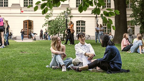 Tre elever sitter på gräsmattan framför Kungstensgymnasiet i Stockholm.