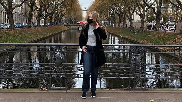 Amelie Anderberg står på en bro i Düsseldorf. Hon har munskydd på sig och har ansiktet vänt från kameran.