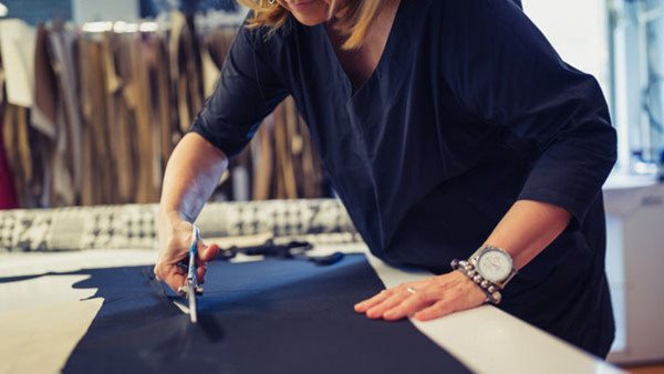 Mature female designer is working in her workshop, cutting material with scissors