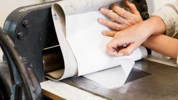 Händer arbetar med tryckpress under grafikkurs på Folkuniversitetet
