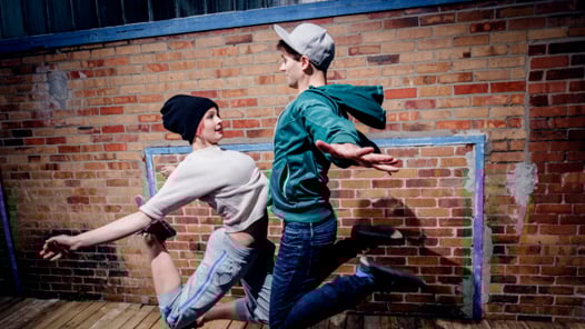 Dansare hoppar framför röd tegelvägg. 