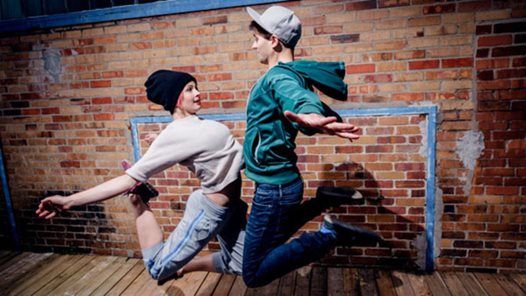 två ungdomar som dansar street och möts i ett hopp framför en tegelvägg