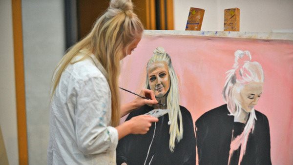 Kvinnlig studerande på Konstnärlig grundutbildning målar vid ett staffli.