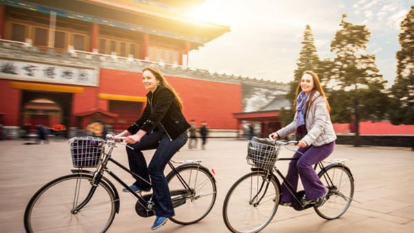 Två kvinnor cyklar förbi traditionell kinesisk arkitektur i solnedgång - gå en kur i kinesiska på Folkuniversitetet