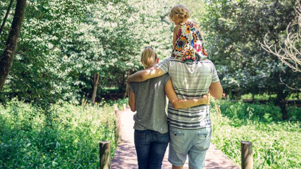 Familj promenerar i grönskande natur - föräldraskap och omsorg i fokus