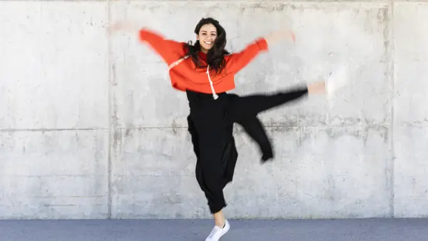 Glad dansare i röd och svarta kläder framför en grå vägg. 