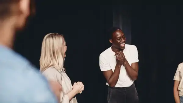 Ung skrattande kille på scen med andra i en teatergrupp. 