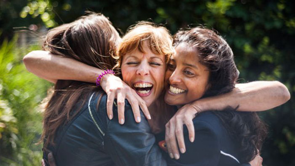 Three women, greeting and hugging outdoors.