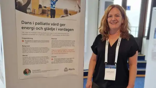 En kvinna som st&aring;r bredvid en affisch i ett rum.