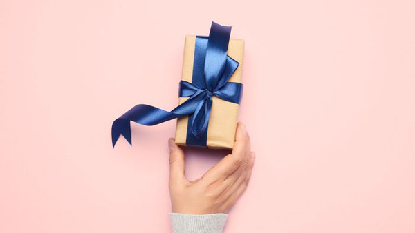 Hand som håller i ett litet paket med blått sidenband - innehåller presentkort från Folkuniversitetet
