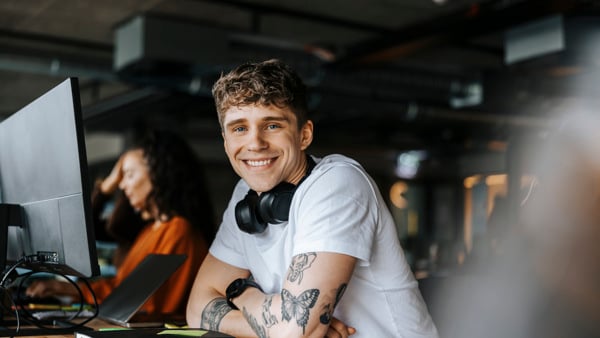 Person i blå tröja som ler mot kameran, datorn är uppslagen och redo