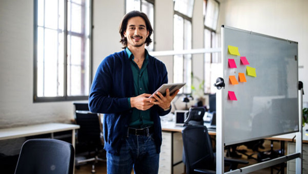 Establishment courses. Portrait of smiling young handsome man standing with digital tablet by whiteboard at creative office.