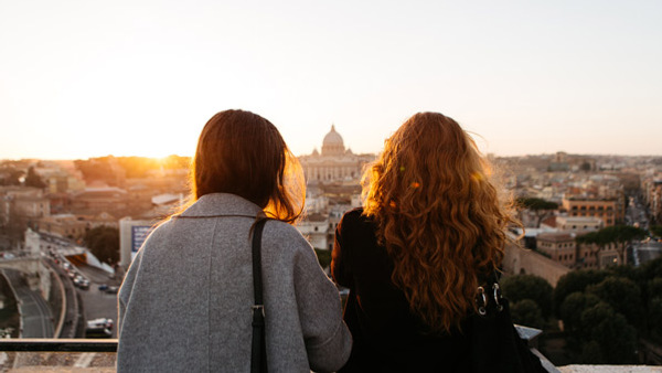 Två kvinnor sitter på en avsats med utsikt över en stad.
