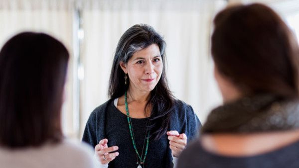 Kvinna talar engagerat med två personer i ett ljust rum - kurs i jiddisch på Folkuniversitetet