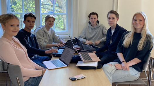 En grupp människor som sitter runt ett bord med bärbara datorer.
