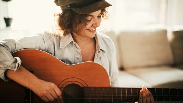 En person med hatt som spelar gitarr.