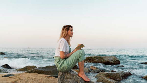 Kvinna sitter vid havet och skriver