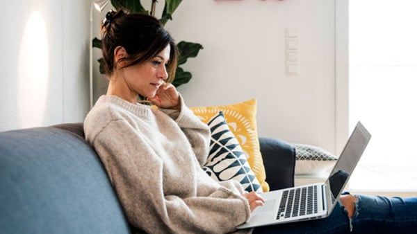 Woman sitting on her couch, surfing the net, using laptop