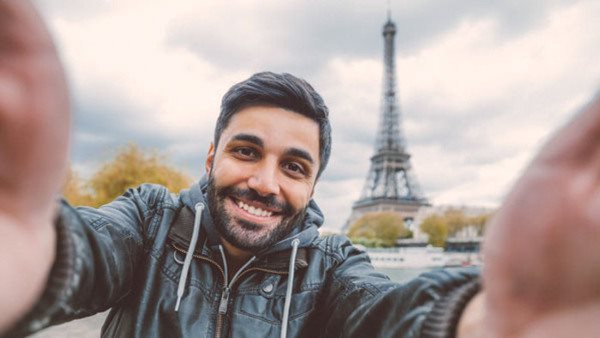Leende man tar en selfie framför Eiffeltornet i Paris under en kurs i franska