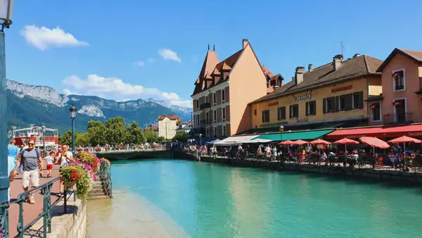 En flod som rinner genom en Annecy med Alperna i bakgrunden. Läs franska i Frankrike.
