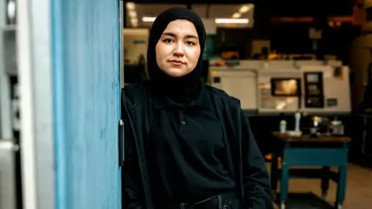 En kvinna i svart hijab som står vid en blå vägg.