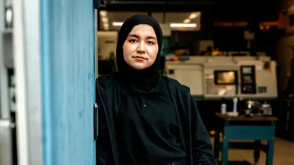 En kvinna i svart hijab som står vid en blå vägg.