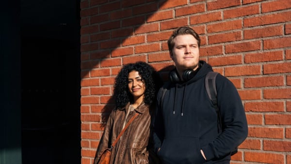 En man och en kvinna står bredvid en tegelvägg.