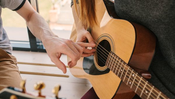 Gitarrlärare visar elev hur man spelar ackord på akustisk gitarr