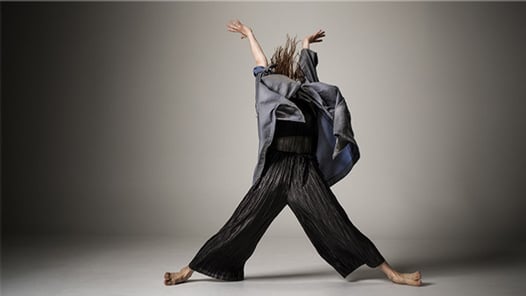 Dansare i fladdrande kläder som täcker ansiktet dansar med händerna upp i luften och benen utåt som ett kryss. 