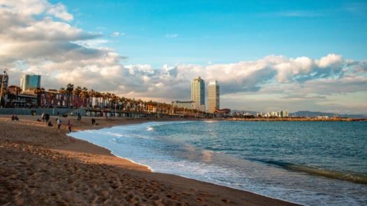 En strand i Barcelona med människor som går på den och byggnader i bakgrunden. Läs spanska i Barcelona med CSN i sommar