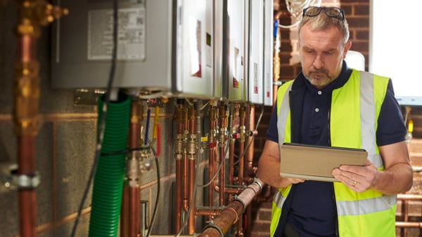 En man med gul arbetsväst kontrollerar vvs-system med en dator i handen