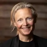 En kvinna med blont hår som ler mot kameran.