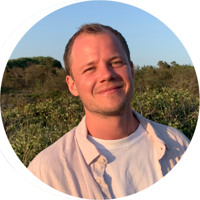 En man i vit skjorta ler mot kameran.