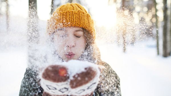 Portrait of happy young woman playing with snow in winter, blowing snowflakes to camera, copy space