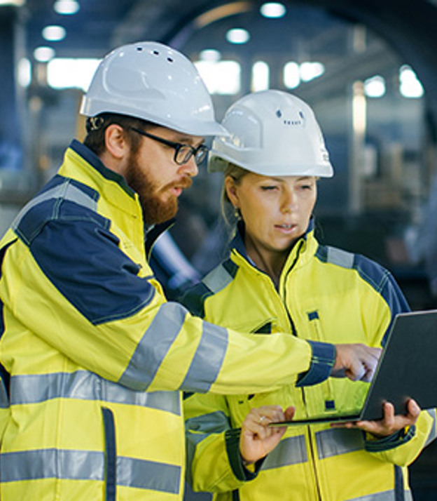 En man och en kvinna i skyddshjälm tittar på en bärbar dator.