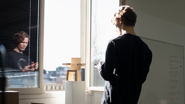 Studerande på utbildningen Produktdesign står vid ett fönster med en modell av en stol.
