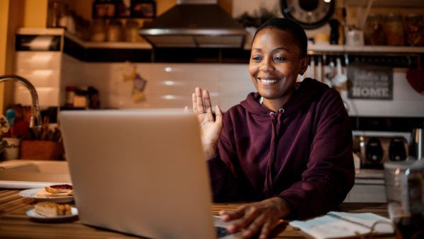 Kvinna framför sin laptop hälsar på sin lärare - Gå en distanskurs i språk hos Folkuniversitetet