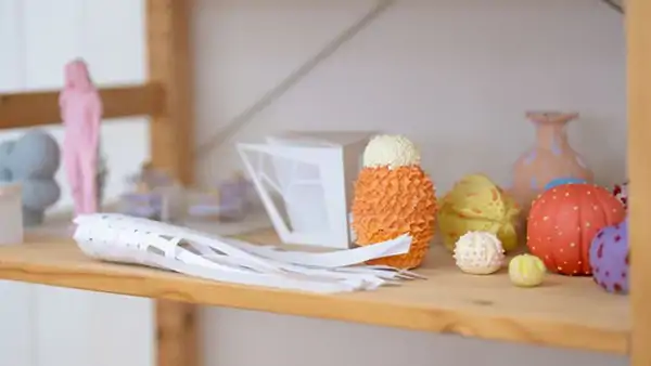 Trähylla med färgglada konstobjekt och modeller i olika former och material. Fokus på kreativitet och detaljrikedom.
