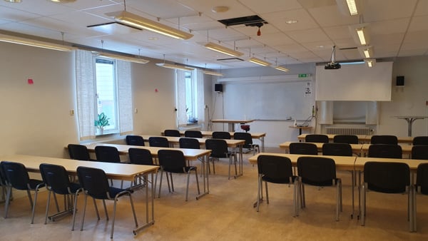 Ett klassrum med bord och stolar och en projektorduk.