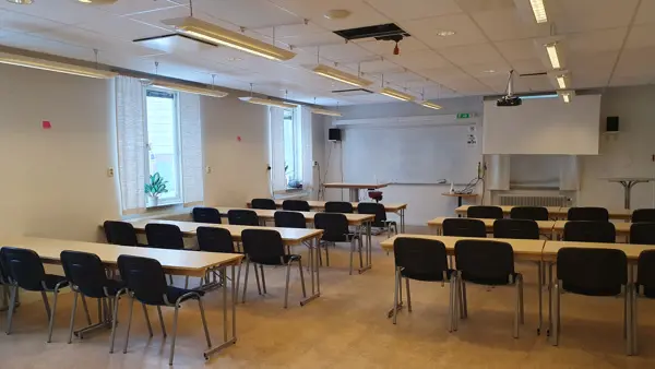 Ett klassrum med bord och stolar och en projektorduk.