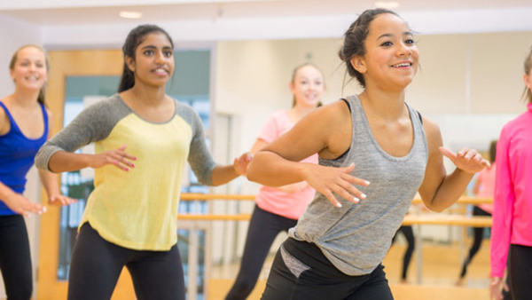 A group of teenage girls are dancing together in a gym studio during a Zumba fitness class.