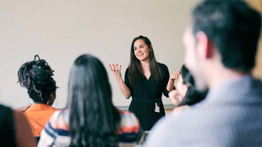 En kvinna håller en presentation inför en grupp deltagare i klassrumsmiljö