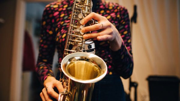 Deltagare i färgglad tröja övar saxofon på musikkurs
