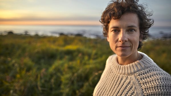 Kvinna står med ett landskap bakom sig. 