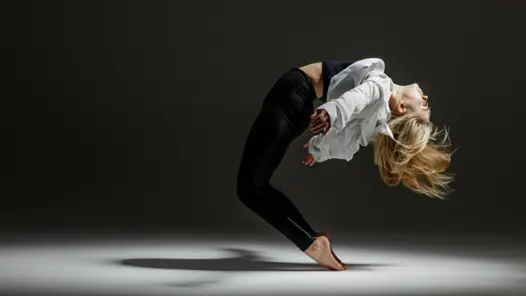 En kvinna i vit skjorta och svarta byxor gör en handstående.