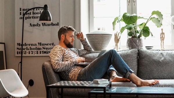 Man i soffa med laptop i knäet - Gå en distanskurs på Folkuniversitetet