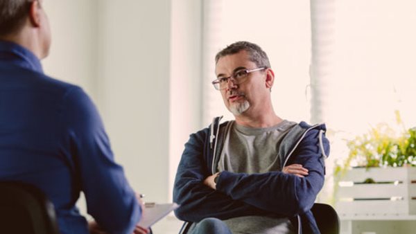 Mature psychotherapist talking with depressed man. Coach is discussing about mental illness with man. They are in meeting in psychotherapeutic office