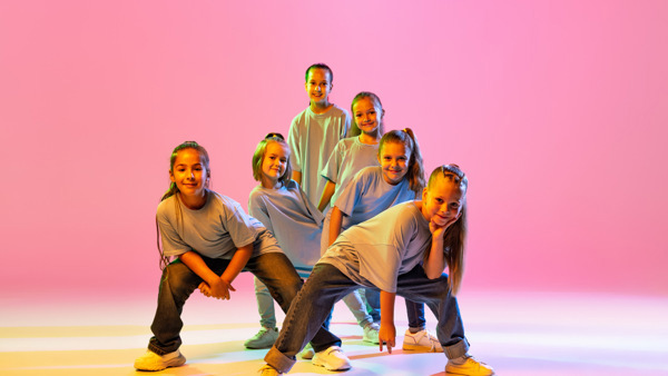 Unga dansare i streetkläder framför en neonrosa bakgrund.