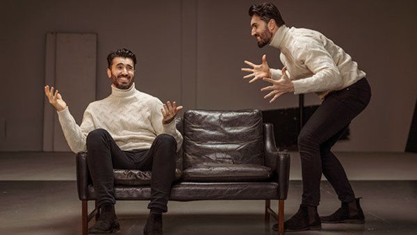 två identiska skådespelare en sitter i en soffa och en står bredvid på Balettakademiens teaterutbildning