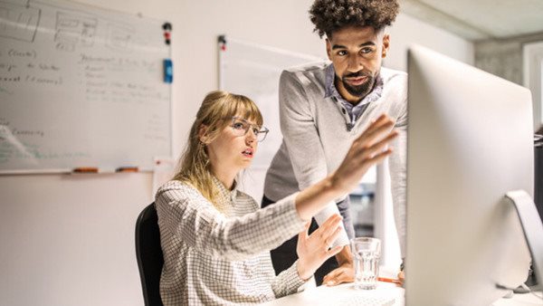 Multi-ethnic businesswoman and businessman discussing over computer at desk in creative office